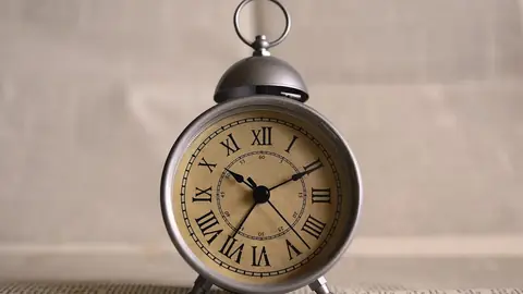 Old metal alarm clock with Roman numerals on a grey shelf