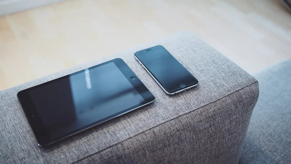 Tablet and smartphone with dark screens lying on a grey sofa